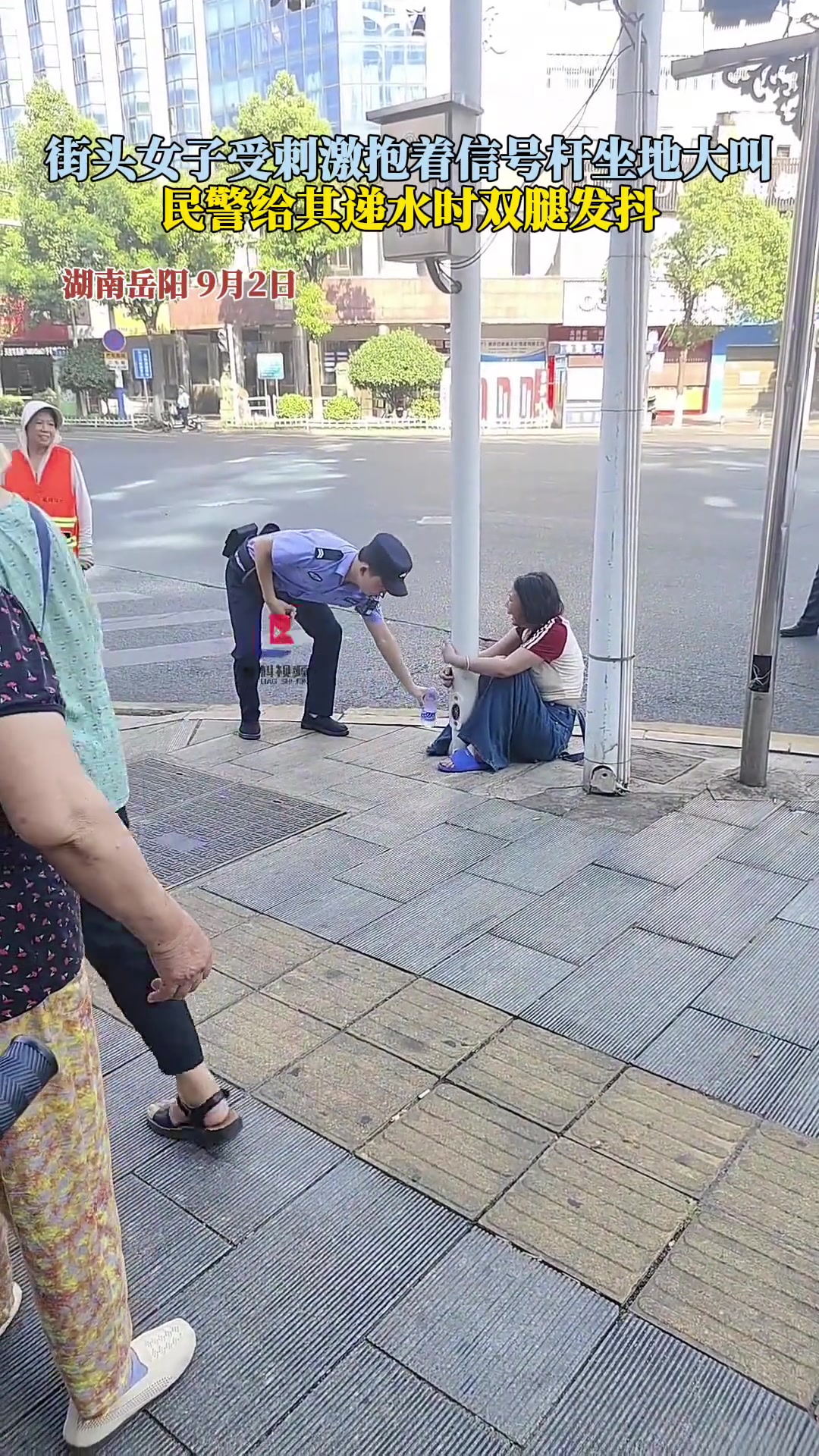 街头女子受刺激抱着信号杆坐地大叫民警给其递水时双腿发抖