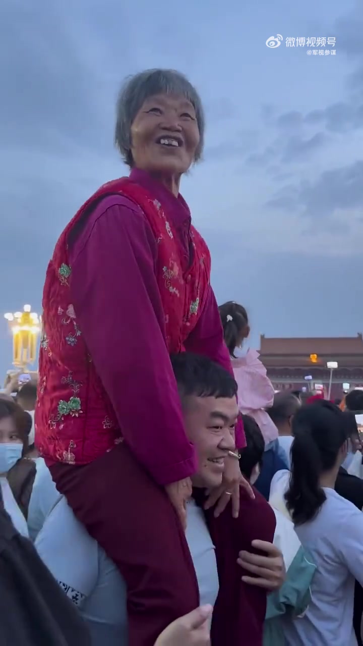 儿子带母亲看国旗，人太多看不见直接将妈妈放到肩膀上扛着