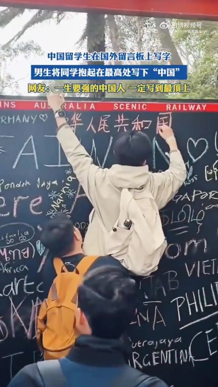 留学生在国外留言板上写字，男生将同学抱起在最高处写下“中国”