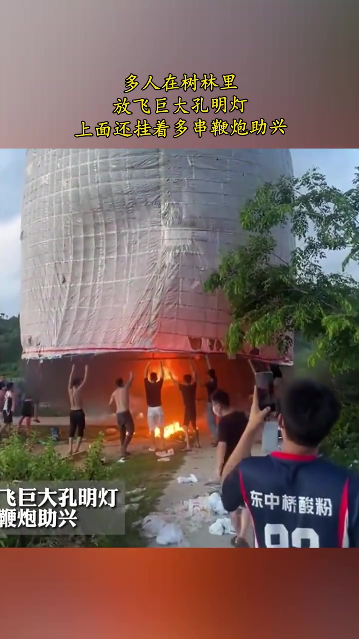 多人在树林里放飞巨大孔明灯，上面还挂着多串鞭炮助兴！
