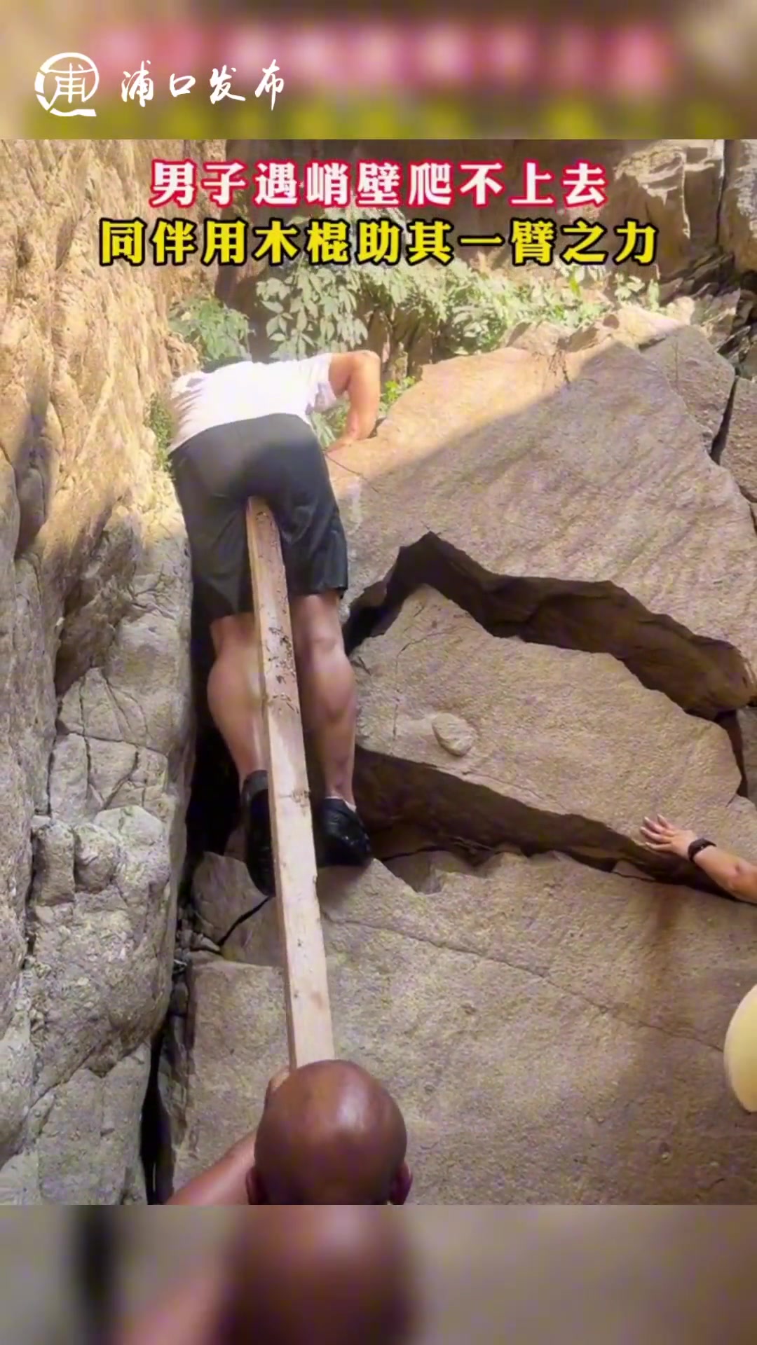男子遇峭壁爬不上去同伴用木棍助其一臂之力