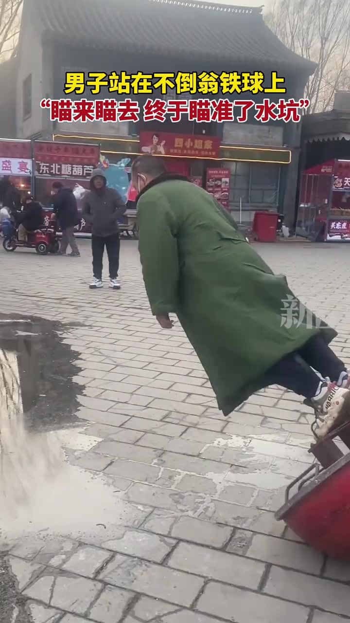 男子站在不倒翁铁球上，“瞄来瞄去，终于瞄准了水坑”