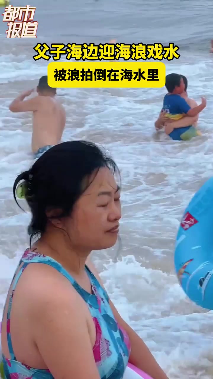 父子海边玩水，被海浪拍倒在水里