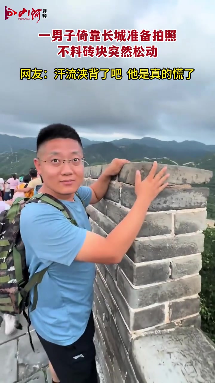 一男子倚靠在长城准备拍照，不料石头突然松动
