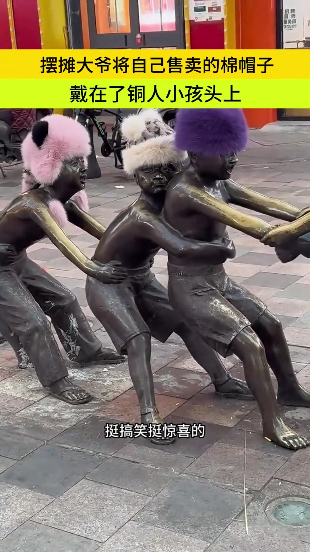 摆摊大爷将自己售卖的棉帽子，戴在了铜人小孩的头上