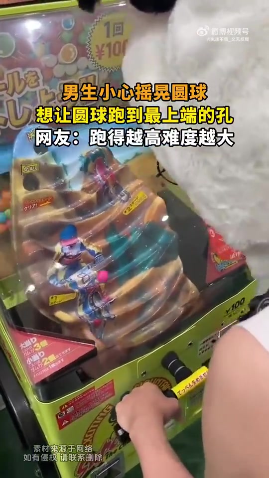 男生小心摇晃圆球，想让圆球跑到最上端的孔！