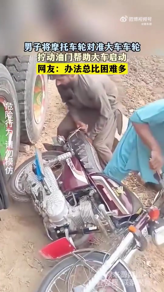 男子将摩托车轮对准大车车轮，拧动油门帮助大车启动