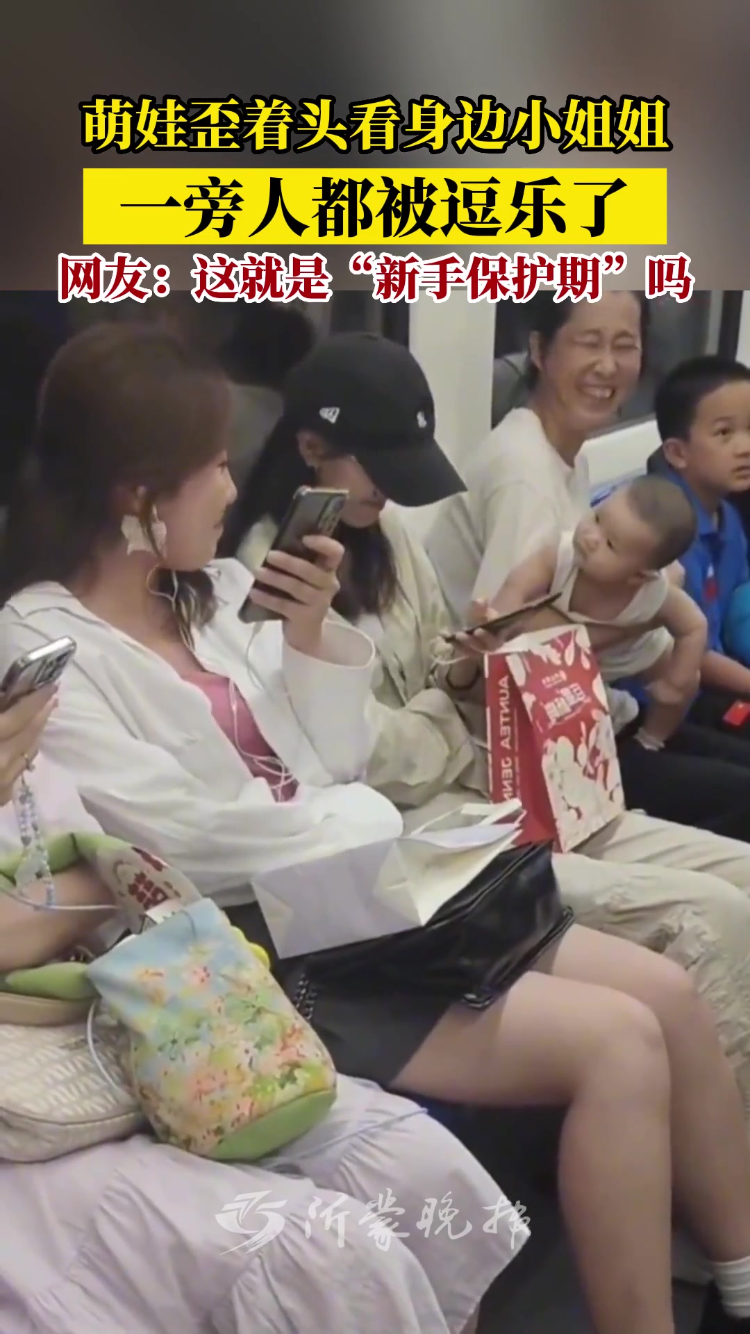 萌娃歪头看旁边的小姐姐，旁边的人都被逗乐了
