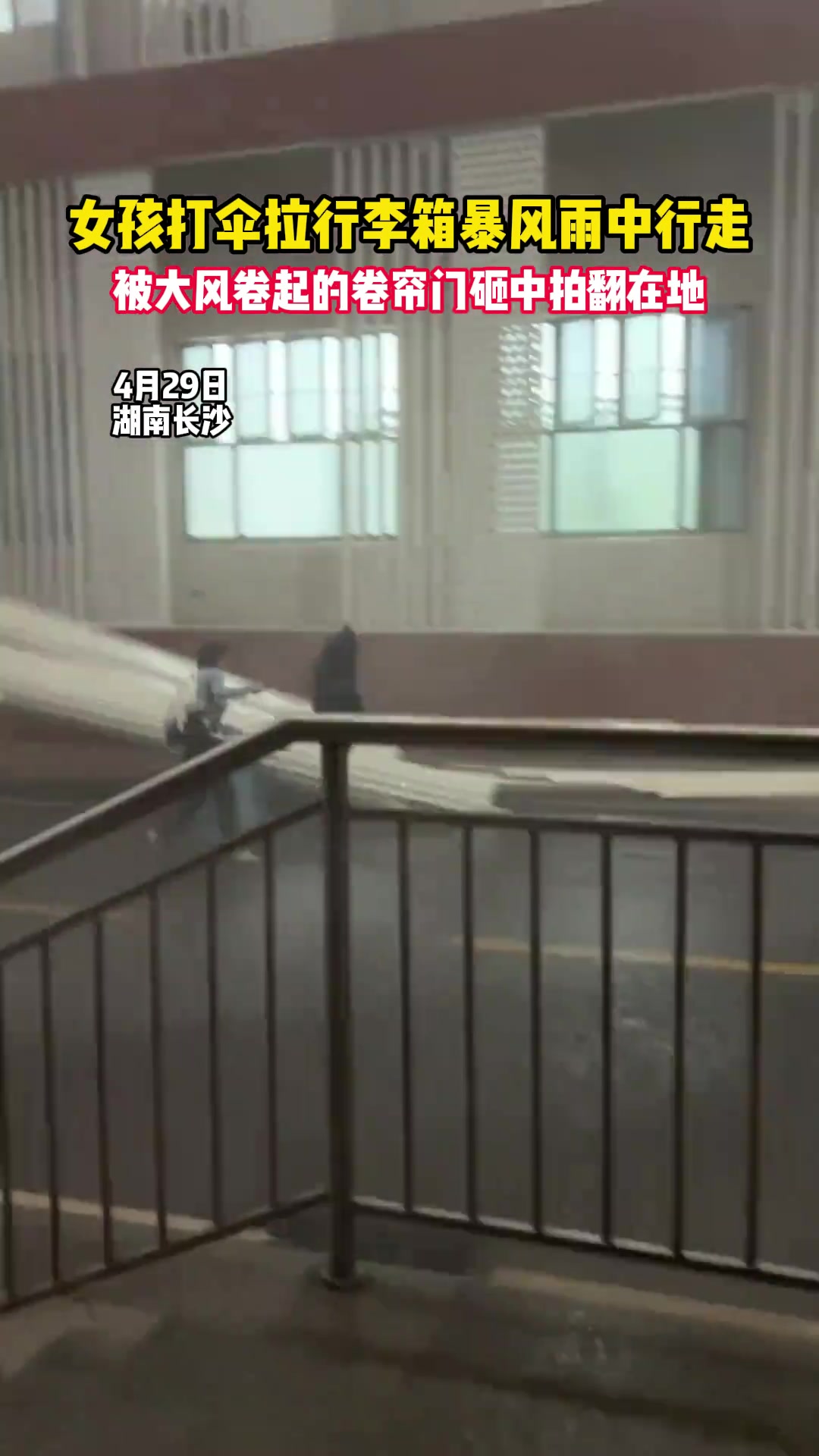女孩打伞拉行李箱暴风雨中行走 被卷帘门砸中拍翻在地