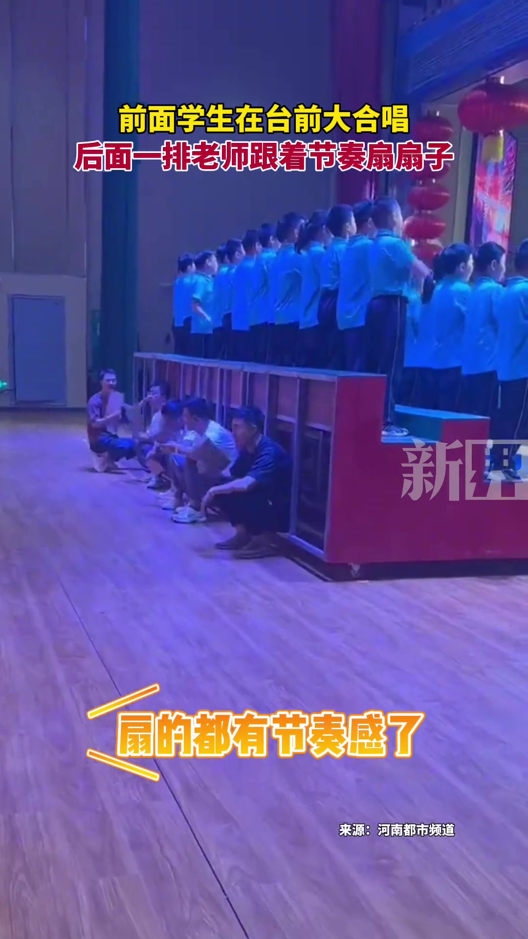 前面学生在台前大合唱， 后面一排老师跟着节奏扇扇子